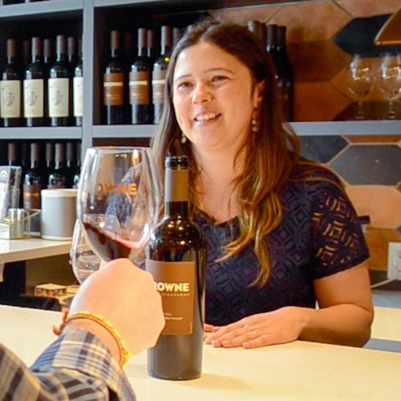 a woman sitting at a table with a bottle of wine