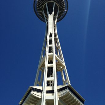 a tall clock tower sitting under a clear blue sky with Space Needle in the background