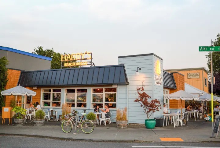 Outdoor view of a cafe with patio seating, bicycles, and a street sign on a sunny day.