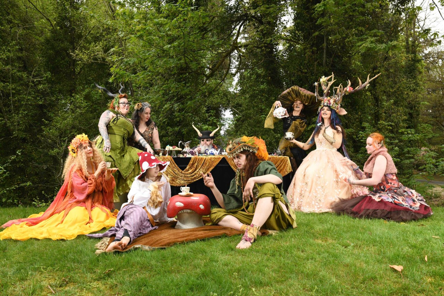 Group in fantasy costumes having tea in a forest setting.