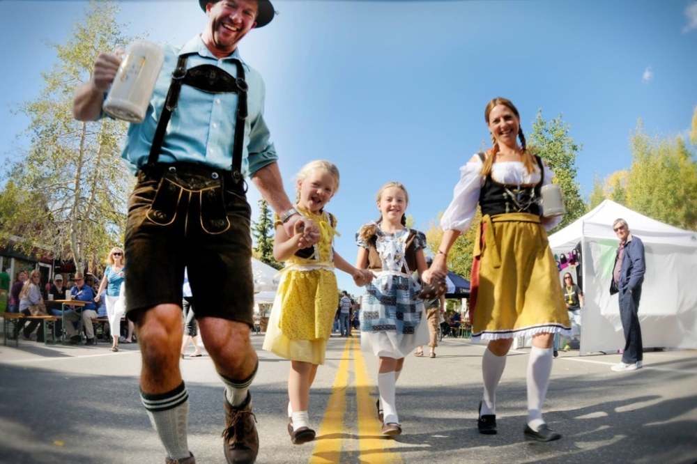 Family in traditional attire walking on a street, holding drinks at an outdoor festival.